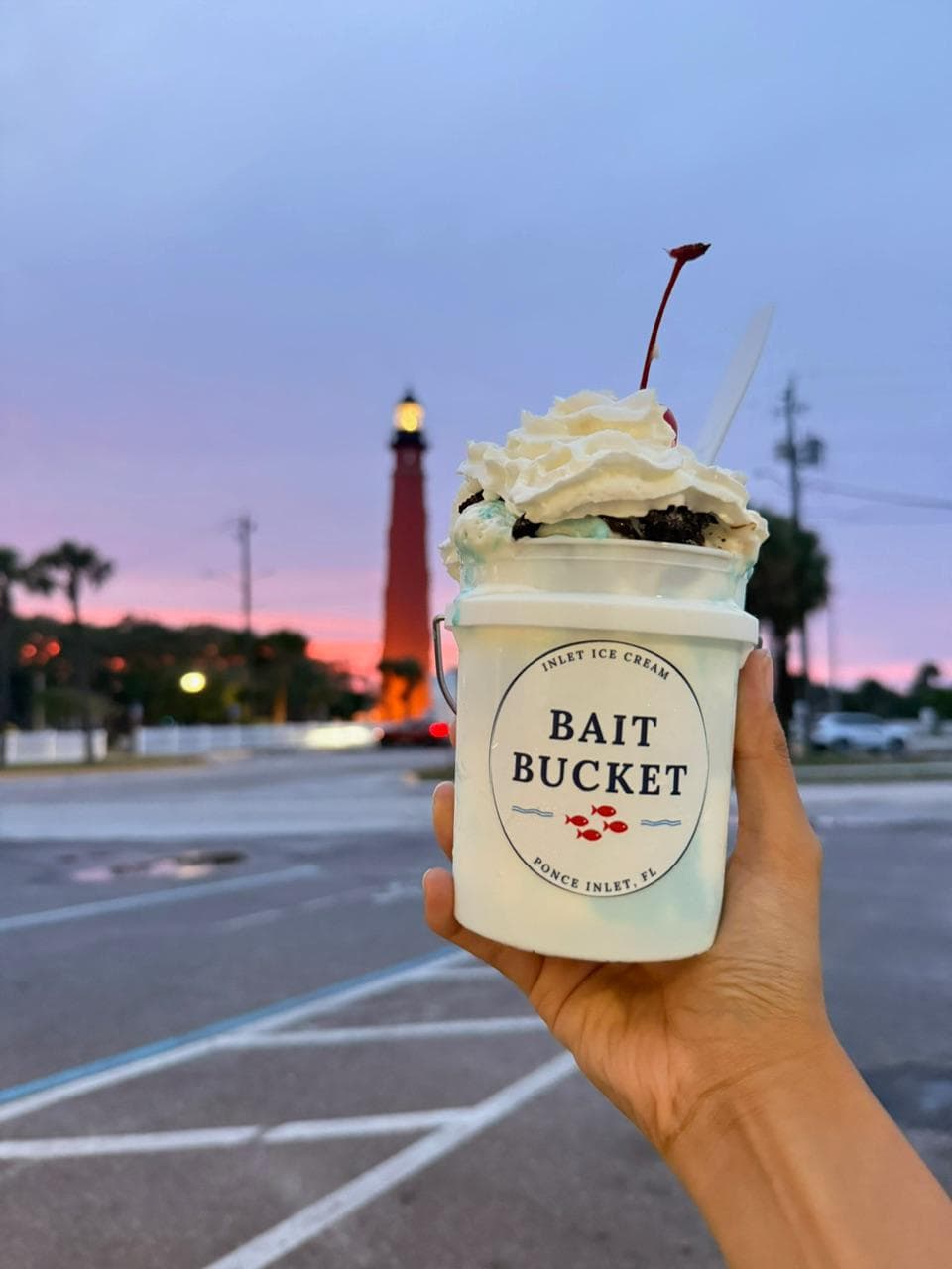 A Bait Bucket sundae held up in front of the Ponce Inlet Lighthouse at sunset.