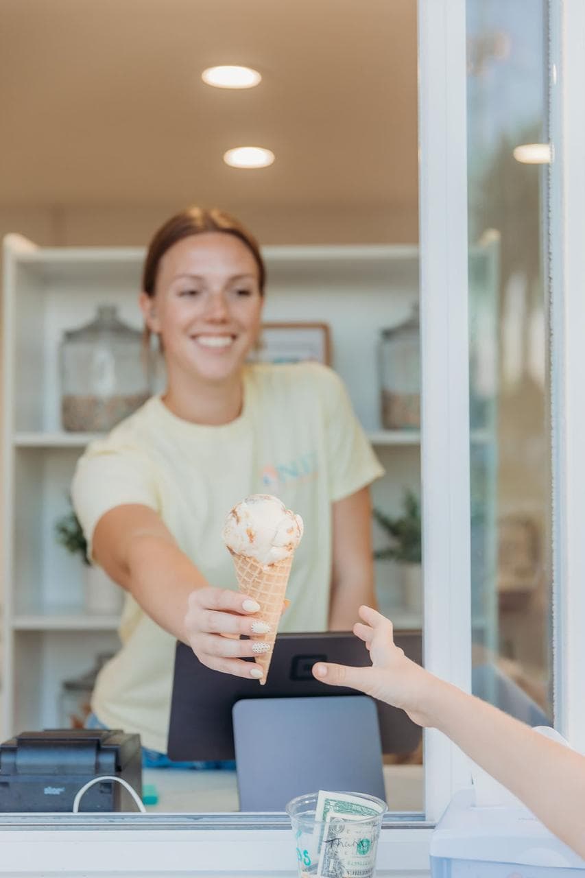 An Inlet Ice Cream server handing a waffle cone through the shop window.